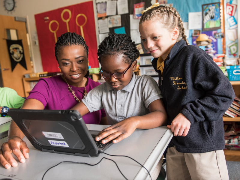Female teacher engages two elementary school students on a tablet computer in a Milton Hershey School classroom.