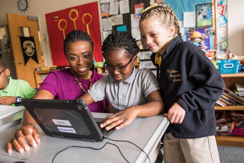 Female teacher engages two elementary school students on a tablet computer.