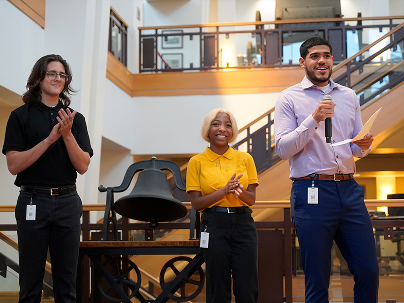Milton Hershey School students Jael Ingram and Rayane El Abdellaoui stand with alumnus Pedro Rodriguez ’18 during a bell ringing ceremony. 
