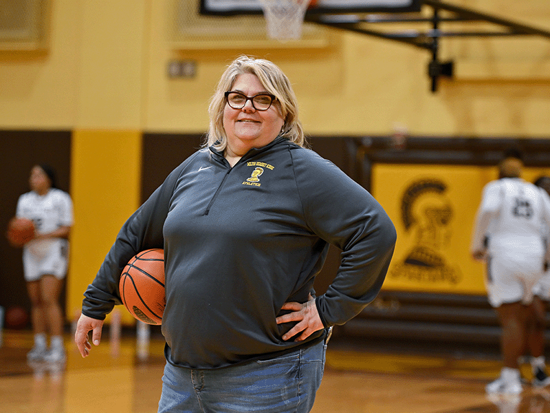 Girls' basketball coach poses with a basketball in hand.