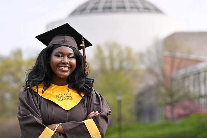 A Milton Hershey School graduate stands in front of Founders Hall.