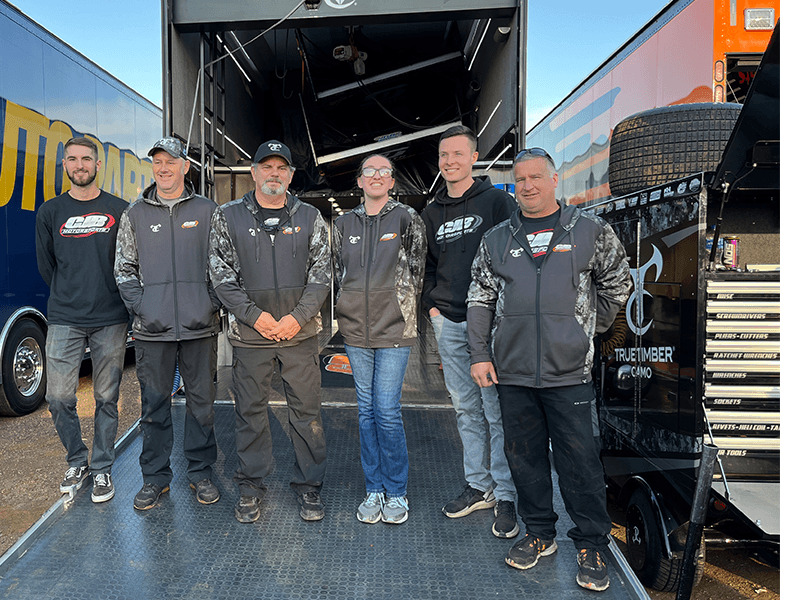 Milton Hershey School student stands with World of Outlaws pit crew and driver.